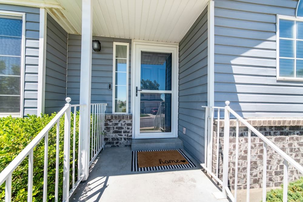 Front porch of a house with blue siding, a glass storm door, white railings, and a doormat that says "home.