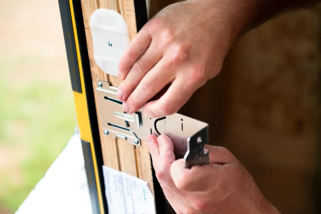 Close-up of a person installing a metal latch plate onto a wooden door frame using a screwdriver.