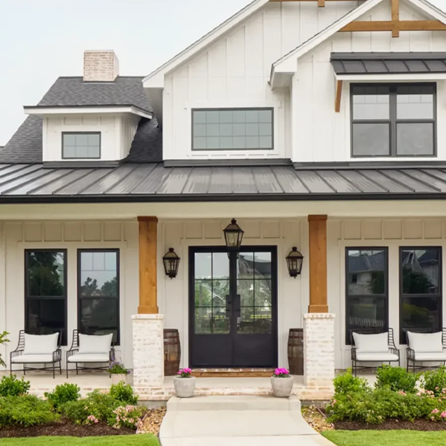 A modern farmhouse-style home with white siding, black trim, wood accents, large windows, double front doors, and a covered porch with seating.