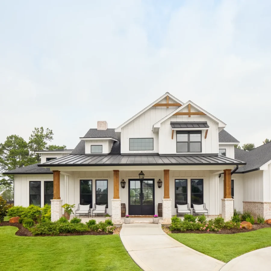 Modern farmhouse with white siding, black trim, front porch with wooden columns, manicured lawn, and a curved walkway leading to double front doors.
