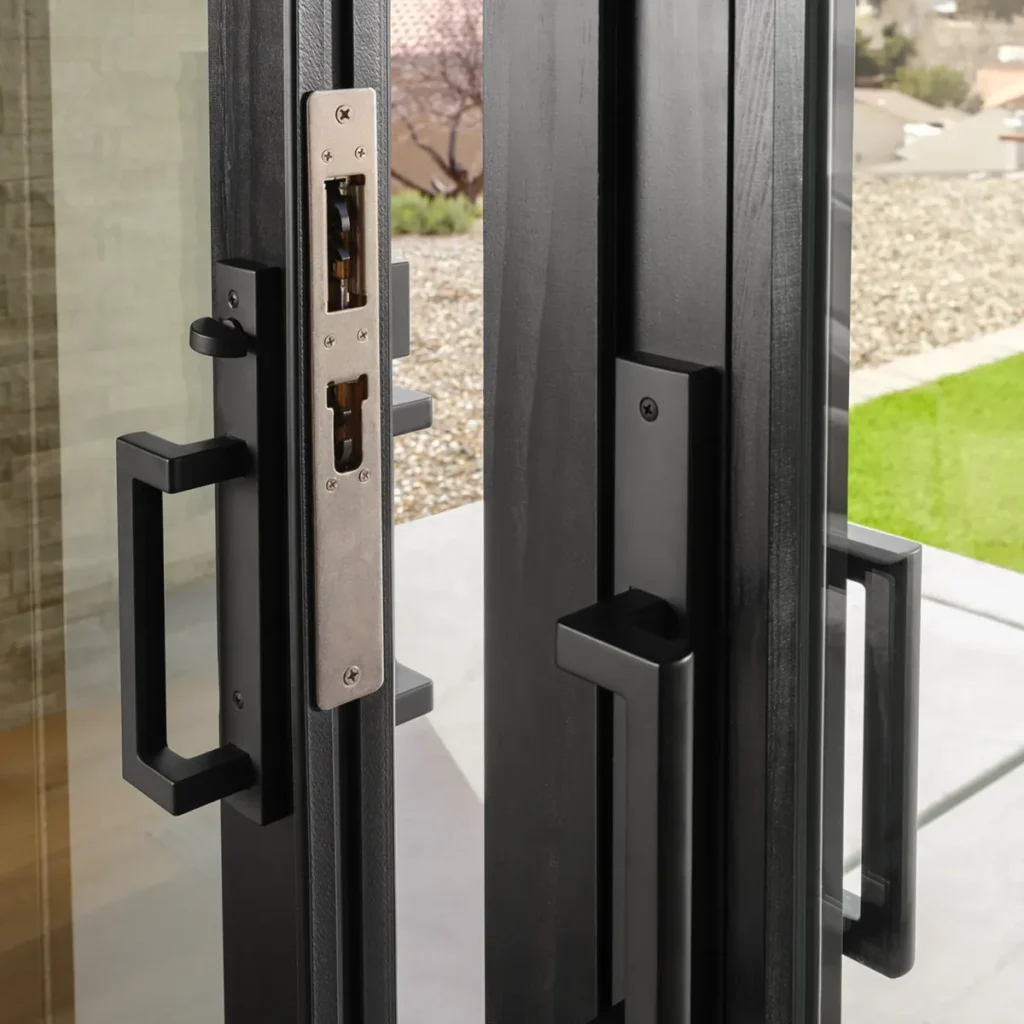 Close-up of modern black metal sliding glass door slightly open, showing the locking mechanism and outdoor patio with grass and gravel.