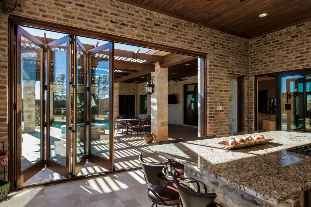 A spacious kitchen with granite countertops opens to an outdoor patio and pool area through large folding glass doors.