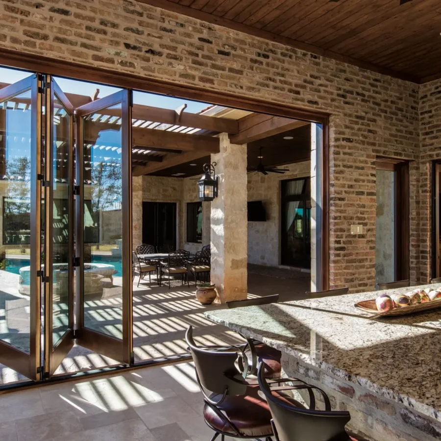 A spacious kitchen with granite countertops opens to an outdoor patio and pool area through large folding glass doors.