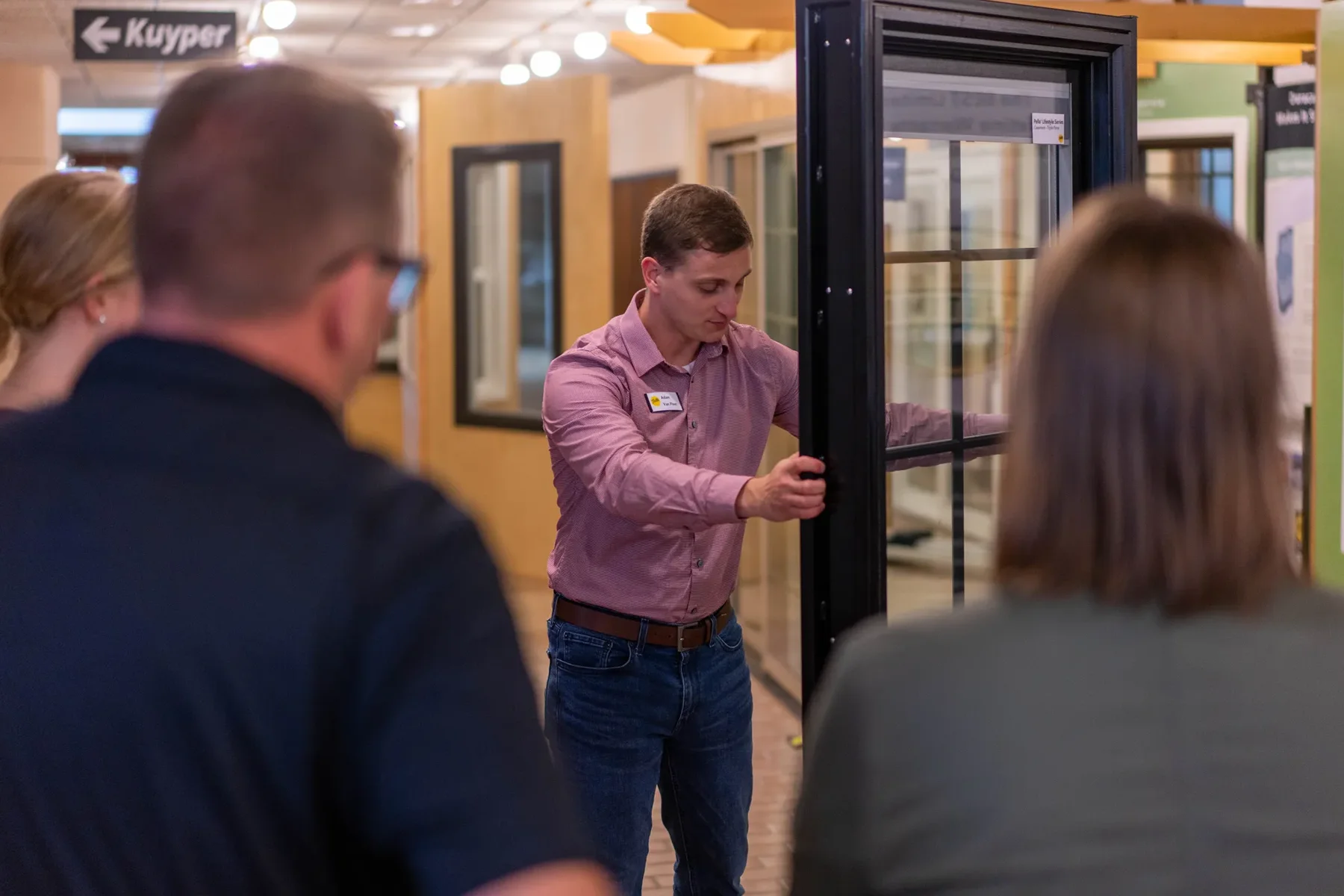 A man demonstrates a window frame to three people in a showroom.