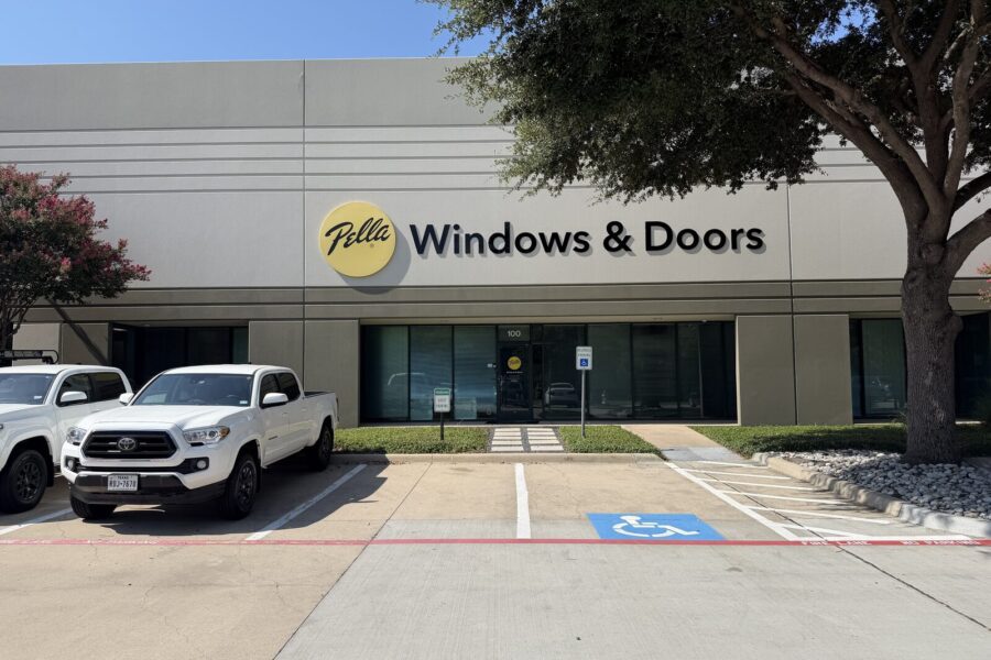 Exterior view of a Pella Windows & Doors storefront with two white vehicles parked in front, including a marked accessible parking space.