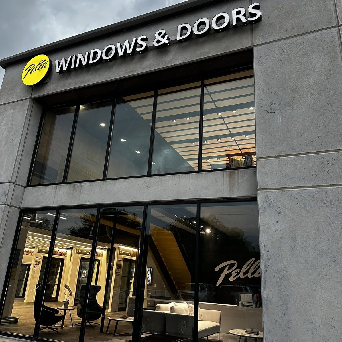 A modern storefront with large windows displays the Pella logo and the words “WINDOWS & DOORS” above the entrance.