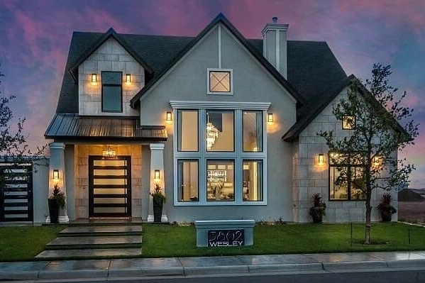 Modern two-story house with large windows, exterior lights on, front lawn, and address sign reading "5900 Wesley" at dusk.