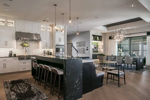 Modern open-concept kitchen with black island, white cabinetry, pendant lights, and adjacent dining area featuring a long table and contemporary chandelier.