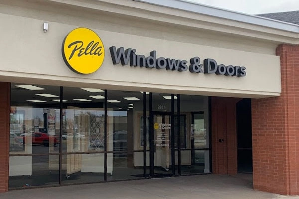 Storefront of Pella Windows & Doors with a glass entrance, yellow logo, and bold signage on a beige and brick building.