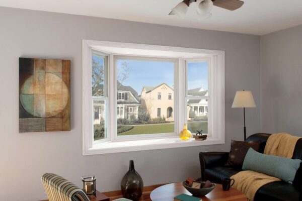 A living room with a large window showing houses outside, a ceiling fan, modern furniture, a round table, and wall art.